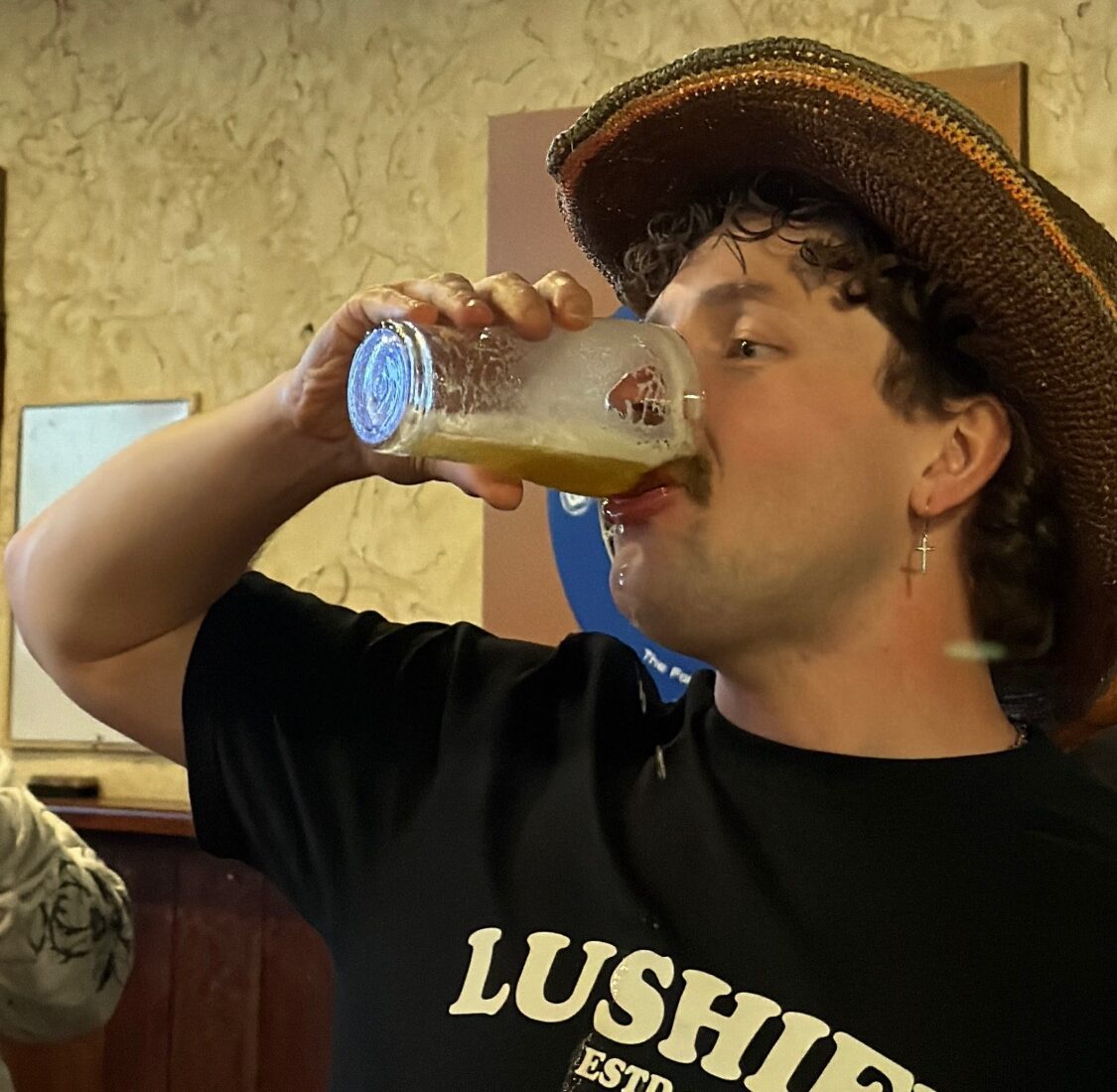 Tyler Lusher in a crocheted hat, skolling a beer on the pub crawl